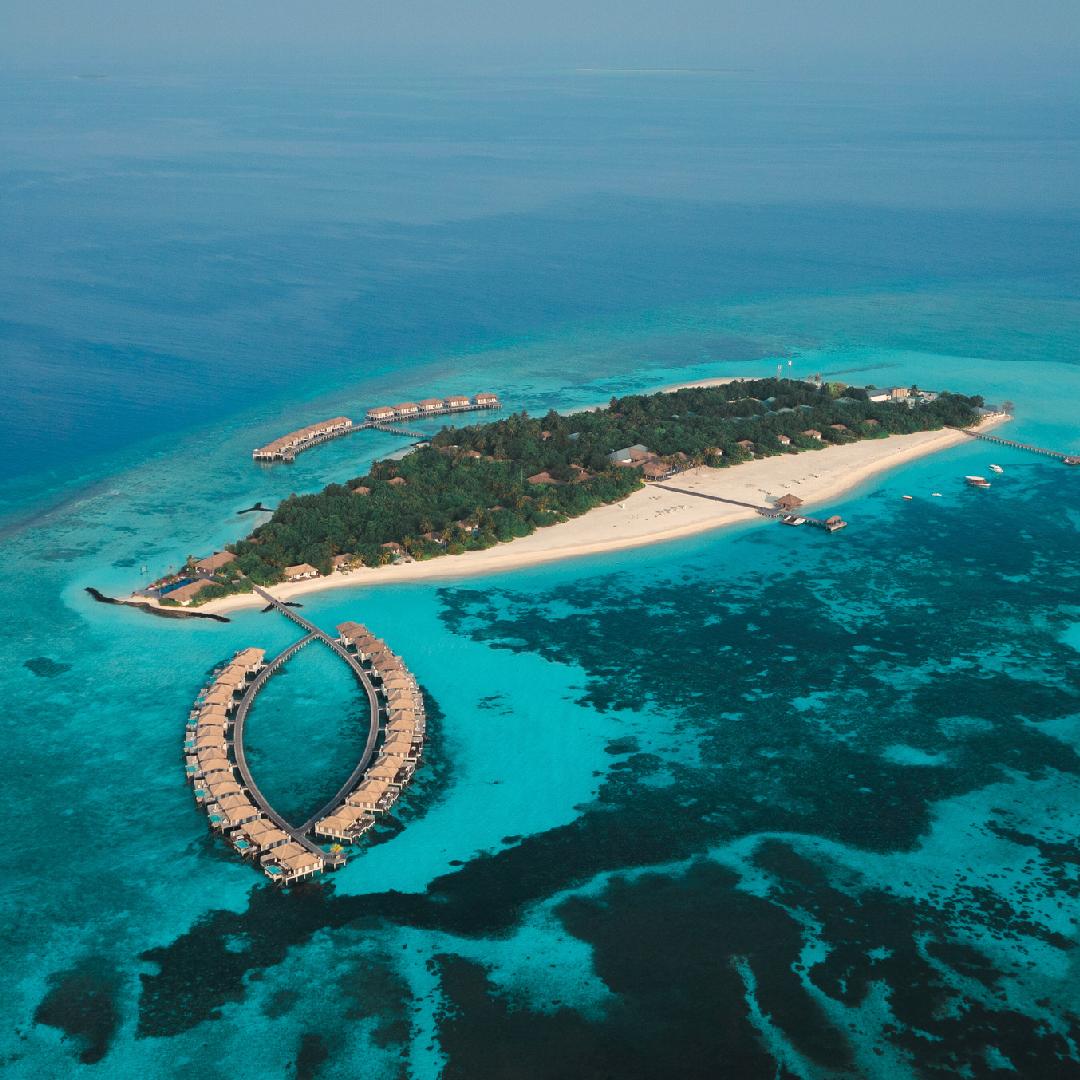 Aerial view of Noku Maldives island and its curved overwater-villa jetties in Noonu Atoll